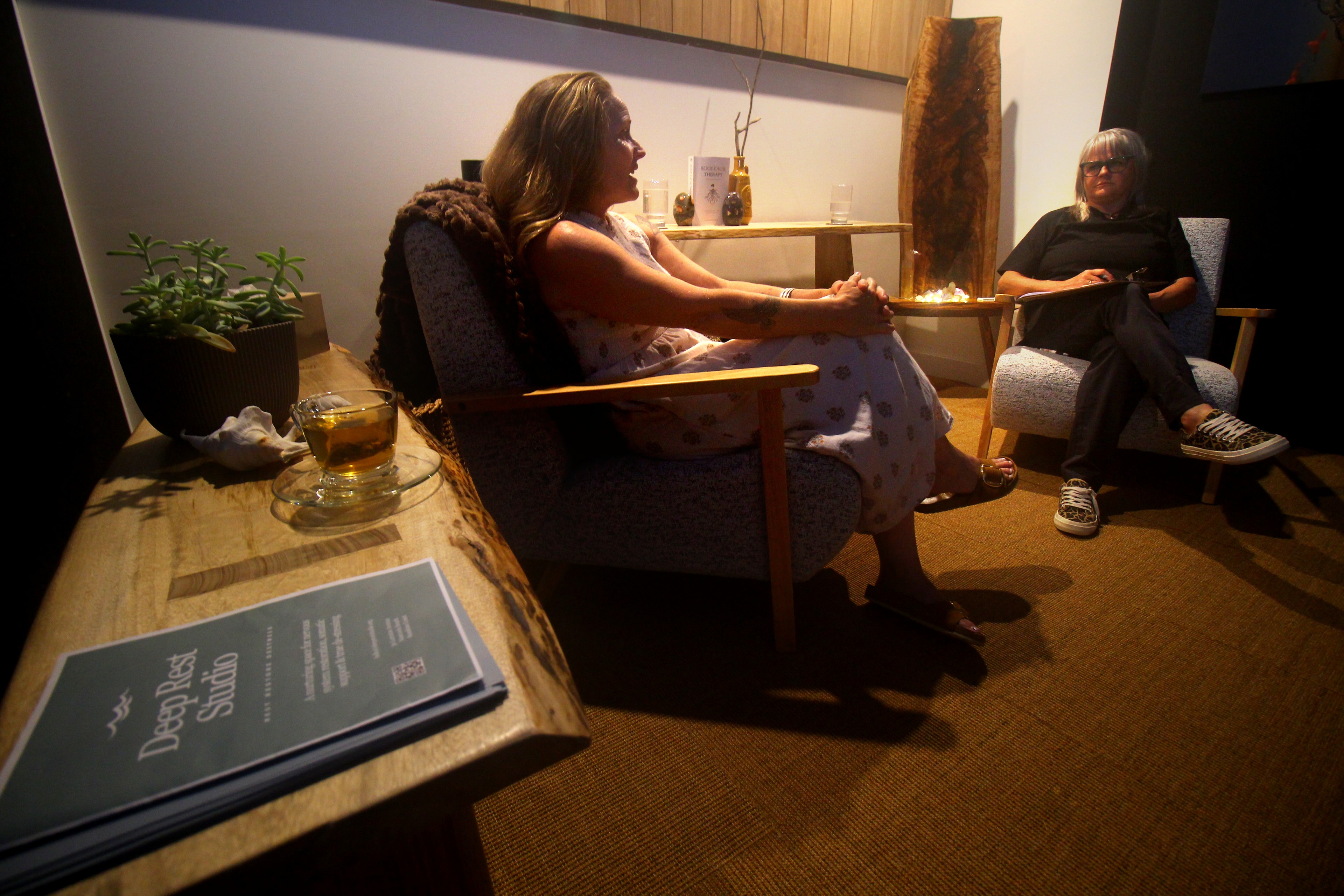 A warm consultation session at Deep Rest Studio — two women seated in comfortable chairs in the softly lit studio space
